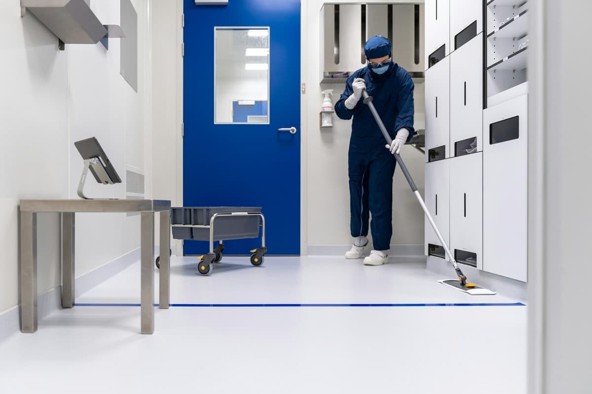 Schoonmaker in beschermende kleding dweilt de vloer van een cleanroom